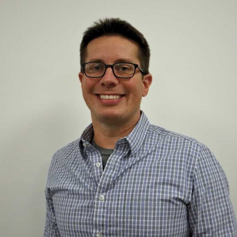 May contain a person smiling with glasses, wearing a checkered shirt.