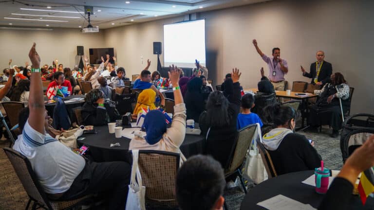 May contain many people in a room with some raising their hands and flags on tables.