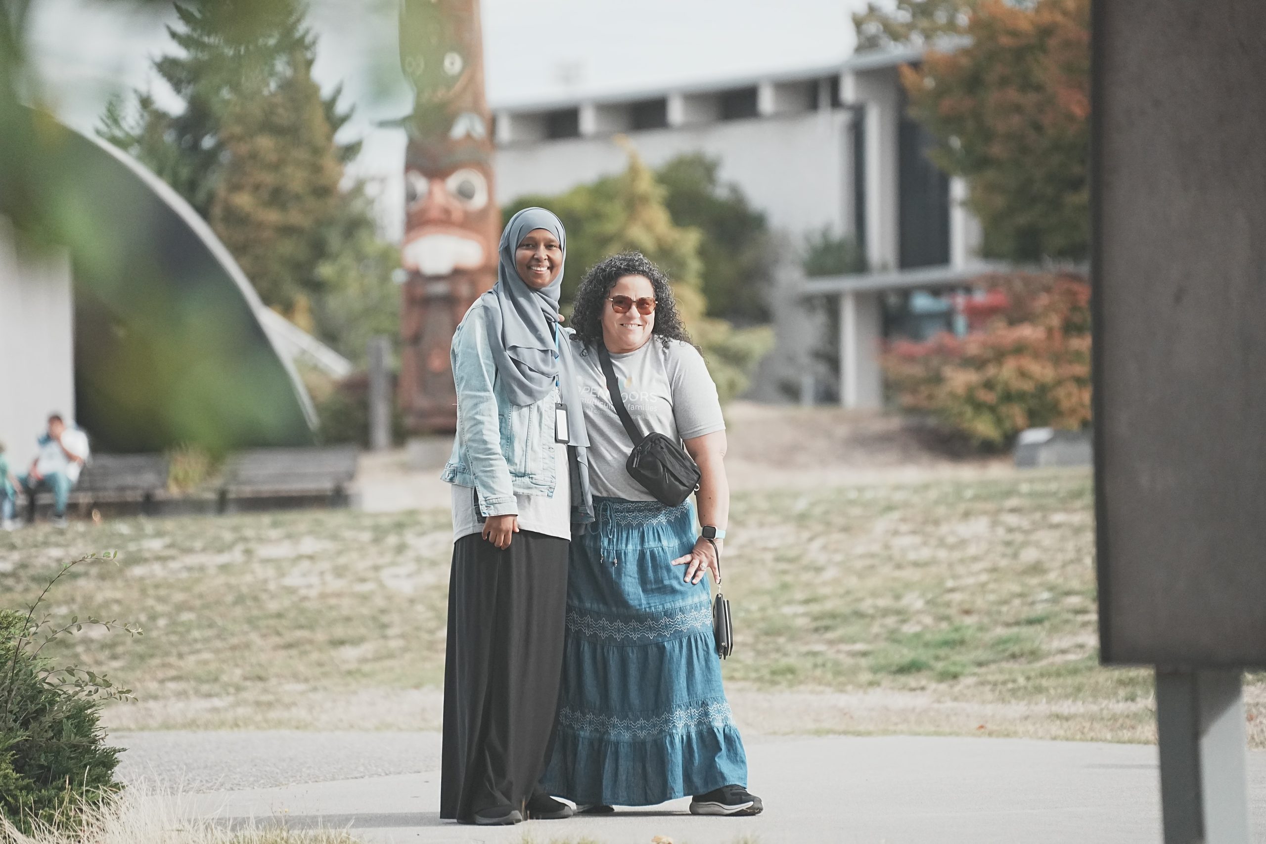 May contain two people smiling, with a totem pole behind them.