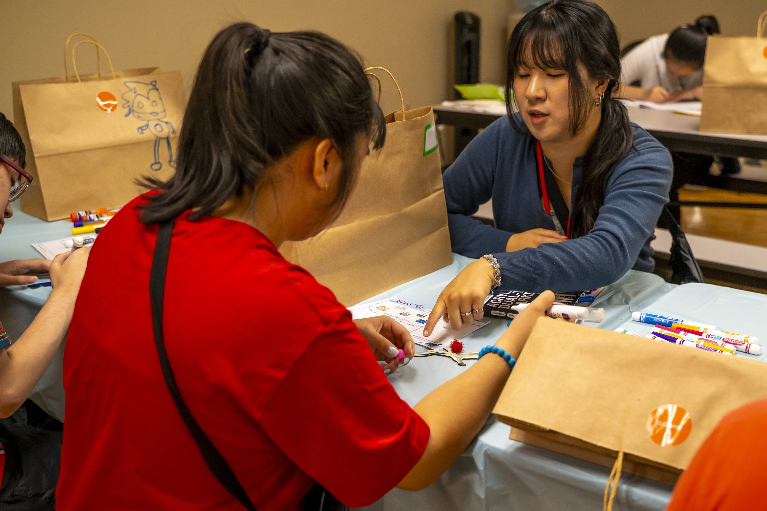 May contain two people working on a craft with markers and paper bags.